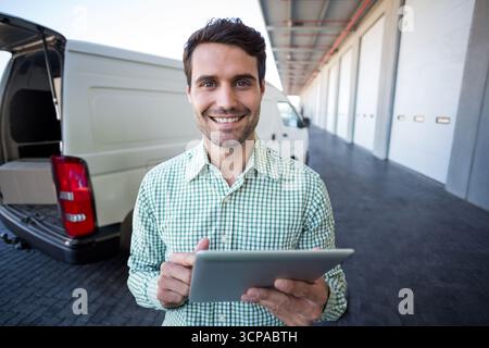 White cargo van waiting at loading dock with open rear doors revealing cardboard box and tablet Stock Photo