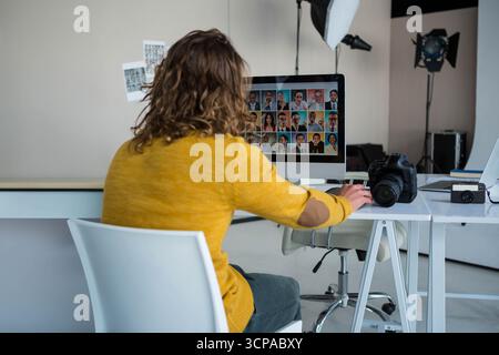 Widescreen monitor displaying headshot grid on desk in studio, with DSLR and compact cameras Stock Photo