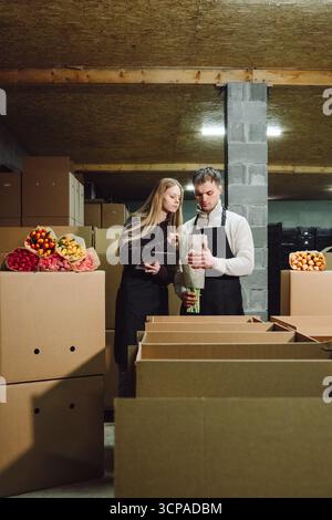 Young couple in a warehouse, inspecting fresh produce while surrounded by cardboard boxes filled with colorful fruits and vegetables, showcasing Stock Photo