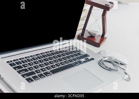 Laptop and hourglass on a desk during a focused work session in a home office Stock Photo