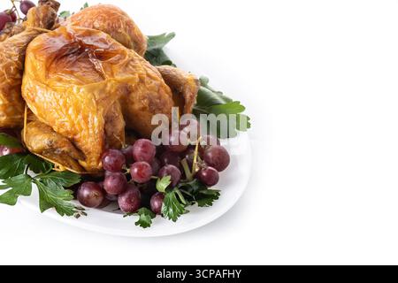 Whole roasted turkey served on a white plate, garnished with fresh parsley and red grapes. Traditional festive meal presentation, isolated on white Stock Photo