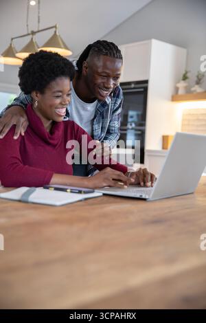 African american couple working on silver laptop and notebook at kitchen table under lights Stock Photo