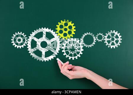 Woman pointing at cogwheels drawn on green chalkboard, closeup. Gear mechanism Stock Photo