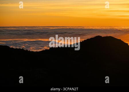 Dramatic sunset over a sea of clouds viewed from a mountain silhouette Stock Photo