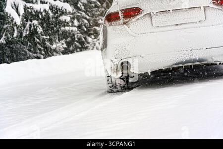 Silver car completely covered with ice parked on snow covered road, detail view to exhaust from behind, blurred trees background empty space for text Stock Photo
