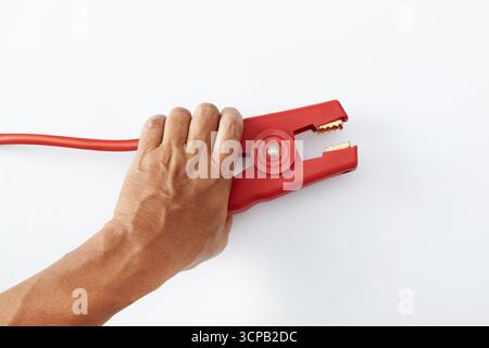 A hand is holding a red jumper cable clamp against a plain white background Stock Photo