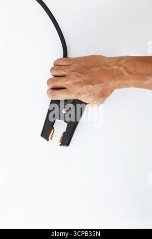 A hand is holding a black jumper cable clamp against a plain white background. Stock Photo