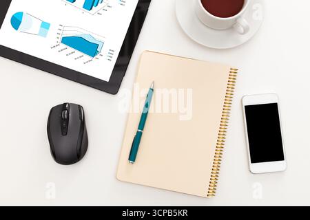 Office workspace with notebook, reports, coffee, and digital devices during busy workday Stock Photo
