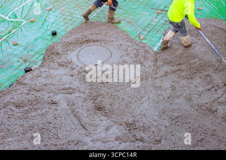 Workers in pouring fresh concrete mix spread for base foundation on construction site. Stock Photo