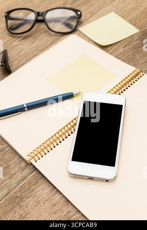 Workspace setup with notebook, pen, smartphone, and glasses during a creative session Stock Photo