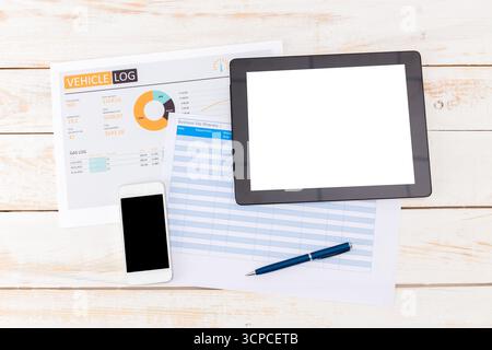 Vehicle log documentation and digital tools arranged on a wooden surface for tracking expenses Stock Photo
