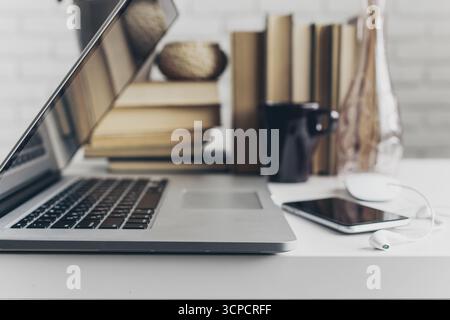 Workstation setup featuring laptop, books, coffee cup, and smartphone near a modern vase Stock Photo