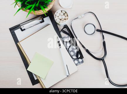 Medical workspace with stethoscope, notepad, and medications arranged on a light wooden table Stock Photo