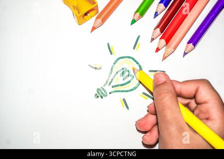 Close Up of Hand Drawing a Glowing Light Bulb with Yellow Pencil for Creativity and New Idea Concept Stock Photo