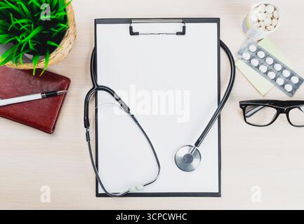 Medical workspace with stethoscope, notepad, and medications on wooden table Stock Photo