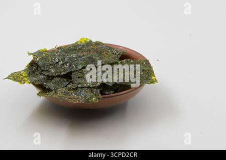 Brown ceramic bowl filled with crispy dried seaweed sheets on a white background. Healthy Asian snack, sushi ingredient, vegan and organic nutrition c Stock Photo