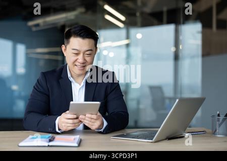 Asian young male businessman sitting in the office at the desk and using a tablet. Stock Photo