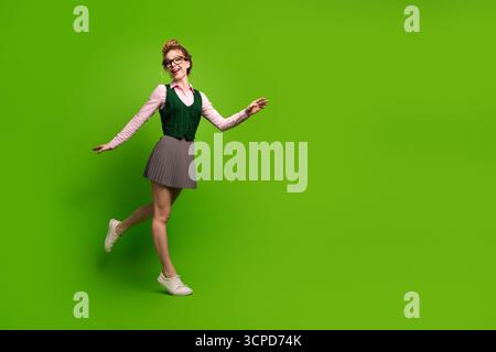Young woman in stylish attire displaying joy and motion against a bright green backdrop, showcasing youthful energy Stock Photo