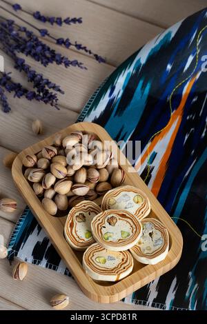 Top view of pistachio halva slices with nuts on a wooden tray, decorated with colorful ikat fabric and scattered pistachios. Ideal for oriental cuisin Stock Photo