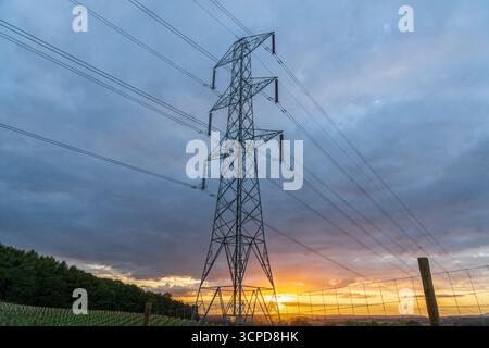 UK Electrical Pylon at sunset, high voltage Power lines part of a modern electricity infrastructure with a colourful sky Stock Photo