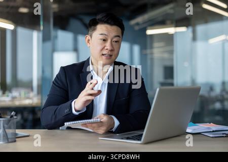 Young Asian businessman holding an online conference in the office, taking notes in a notebook. Stock Photo