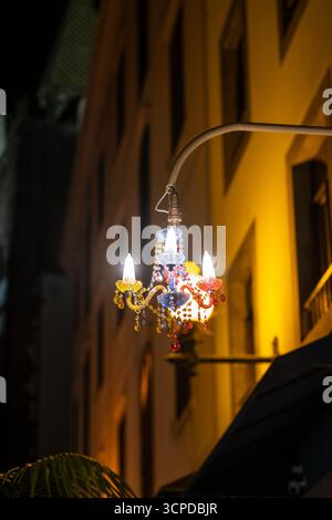 A charming, multi-colored chandelier-style light fixture, adorned with sparkling beads and pendants, hangs illuminated at night, providing decorative Stock Photo