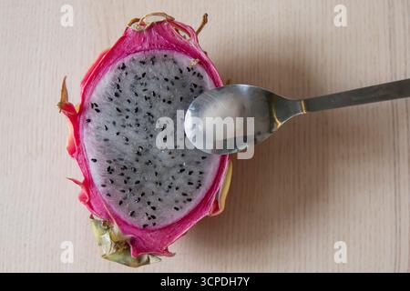 Close-up of half dragon fruit with silver spoon placed on a light wooden background. Exotic tropical pitaya with juicy white pulp and black seeds. Con Stock Photo