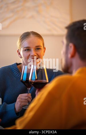 Embarrassed woman clinking wine glass with man on romantic date indoors, intimate time with partner Stock Photo