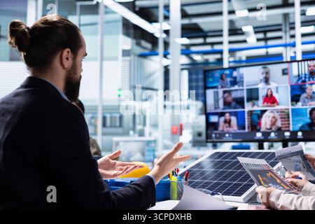 Photovoltaics factory admins look over schematics during internet video call, planning work inside facility. Solar panels plant engineers look over assembly lines blueprints in remote videoconference Stock Photo