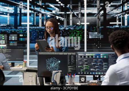 Data center computer scientist uses AI visualization program to oversee automated repetitive tasks. Woman in server hub modifying infrastructure rigs systems based on data analytics graphs Stock Photo