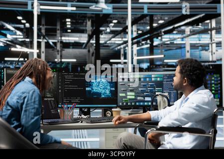 Engineer with paraplegia and coworker setting up data center equipment needed to run artificial intelligence and machine learning. Server room worker with disability and colleague using AI tools Stock Photo