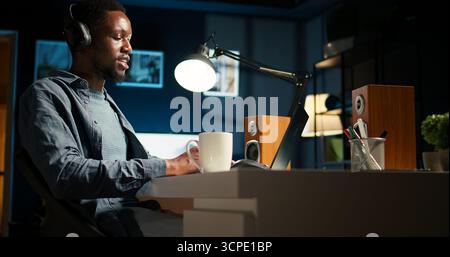 Young focused freelancer attending an online meeting from his home office, discussing with associates remotely. Smiling black man engages in virtual communication, remote technology. Camera A. Stock Photo