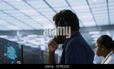 Computer scientist putting headphones on in server room, working to ensure minimal downtime. Engineer using audio device to hear podcasts in data center, monitoring performance, camera A Stock Photo