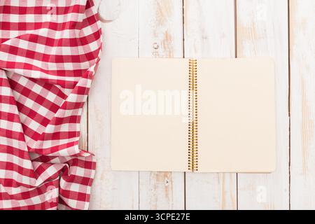 Red and white checkered cloth beside an open spiral notebook on a wooden table Stock Photo
