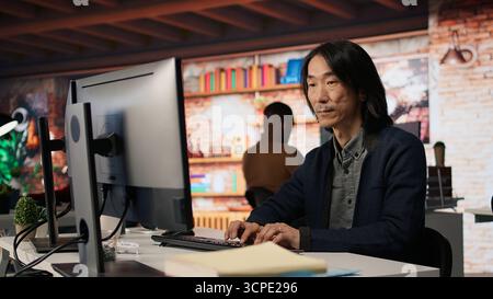 Startup manager leveraging machine learning technology in office to gain competitive edge. Asian Silicon Valley company IT expert working on rapid technological advancement, camera A Stock Photo
