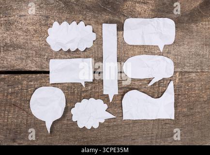 Paper speech bubbles arranged on wooden surface with a rustic feel during daylight hours Stock Photo