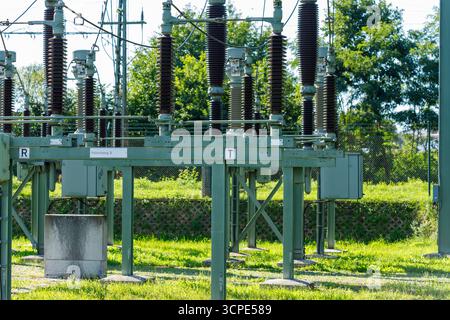 Electrical substation equipment with insulators and metal supports, situated on green grass with trees in the background. Stock Photo