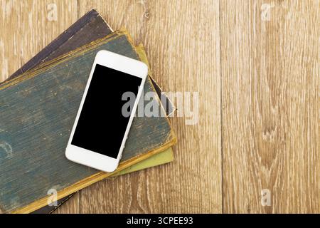 Smartphone placed on stack of old books on wooden table in cozy indoor setting Stock Photo