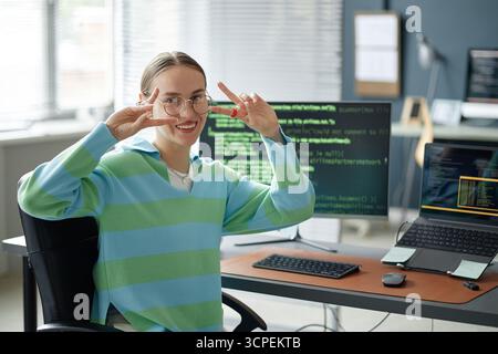 Portrait of Young Woman Smiling and Gesturing Peace Sign at Desk Stock Photo