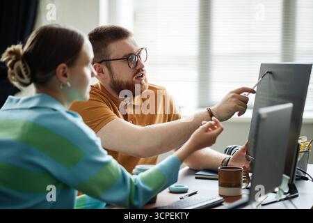Young Adult Man Explaining Computer Code to Young Adult Woman Stock Photo