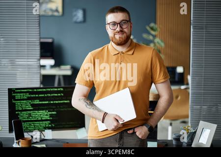 Portrait of Young Adult Man Holding Laptop Standing in Office Stock Photo