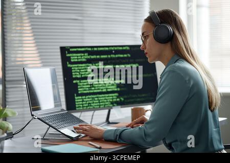 Young Adult Woman Writing Code on Laptop While Wearing Headphones Stock Photo
