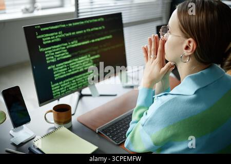 Young Woman Analyzing Code on Computer Monitor in Modern Office Stock Photo