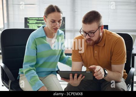 Young Man and Woman Collaborating on Digital Tablet in Office Setting Stock Photo