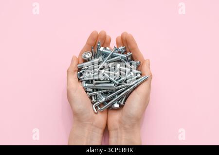Female hands holding pile of different tap bolts and screws on pink background Stock Photo