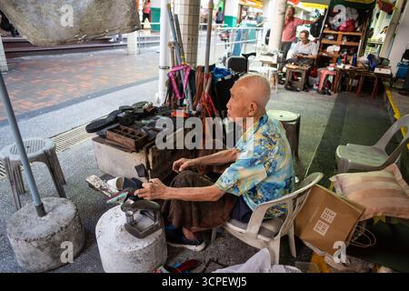 Chinese elderly cobbler repair shoes on the street under shelter, old man working in his late 80s. Dying trade scene, Chinatown, Singapore. Stock Photo