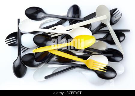 A pair of yellow plastic spoons and forks among a pile of black and white plastic spoons and forks Stock Photo