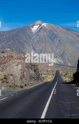 Straight asphalt road leading towards Mount Teide, Tenerife, Spain, cutting through volcanic terrain. Clear blue skies and bright sunlight Stock Photo