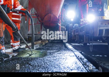 Construction workers pouring concrete under strong lighting, industrial atmosphere and safety equipment, construction of the Hermann Hesse railway, Ca Stock Photo