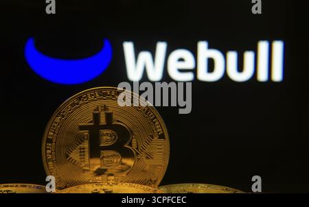 Dhaka, Bangladesh- 04 April 2025: Close-up of Bitcoin coins with the webull logo visible on a screen in the background Stock Photo